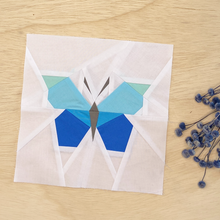 A quilt block, made from paper piecing, with white background fabric and a butterfly in shades of blue and green.